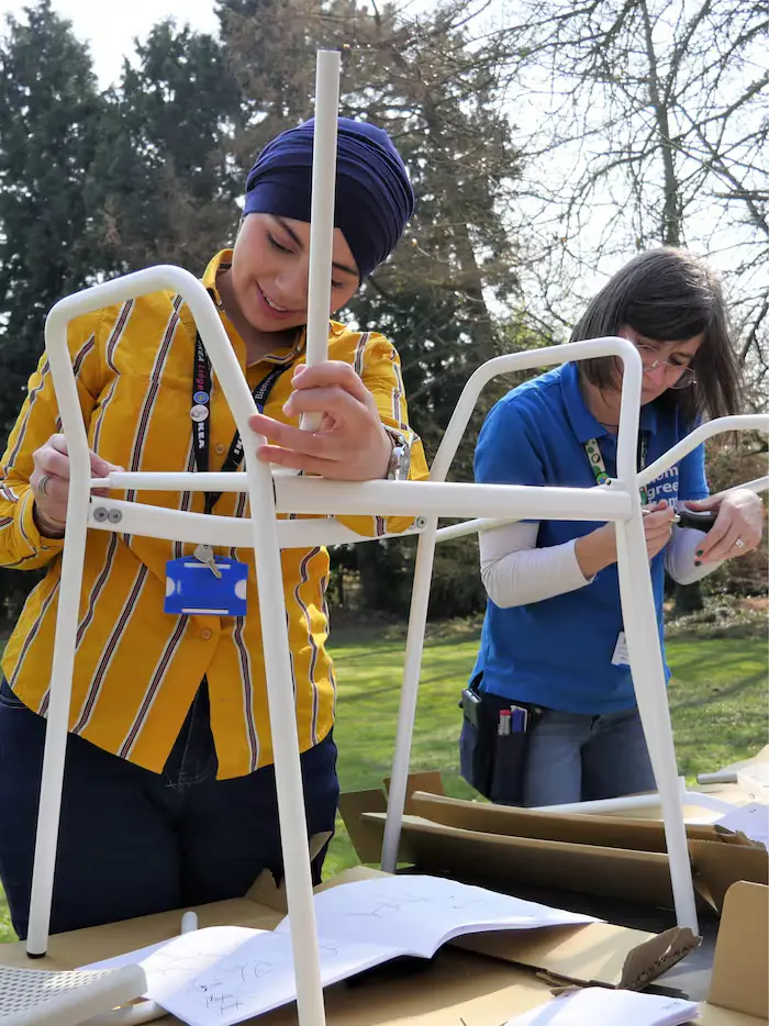 IKEA employees during volunteering activity day. Two women wearing IKEA's branded clothing are outside, assembling a white chair.